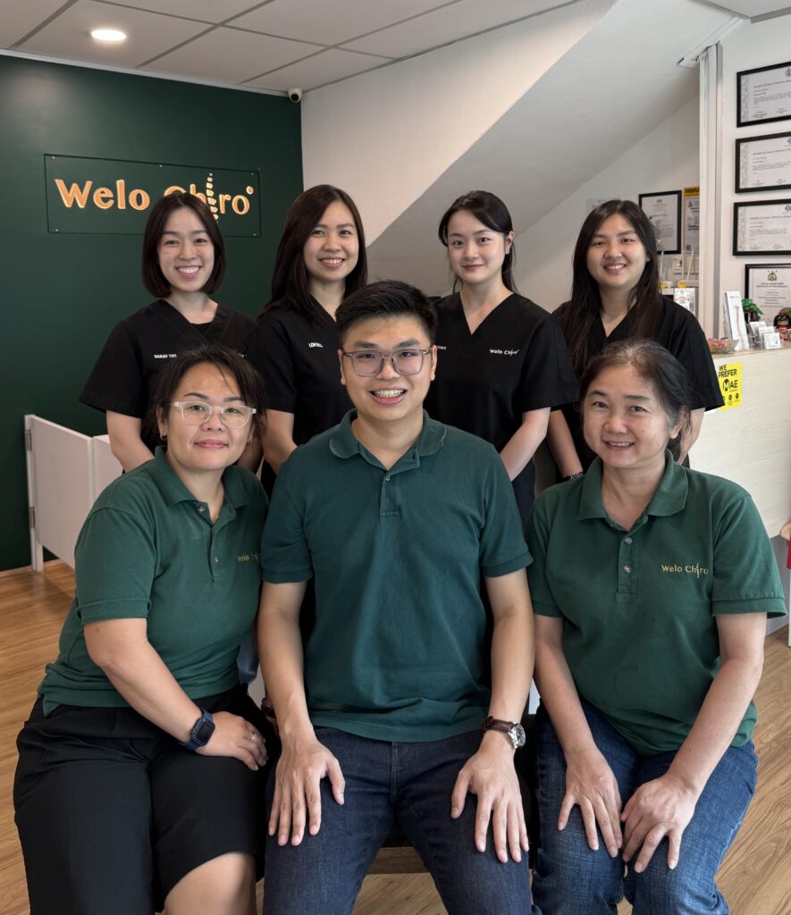 The Welo Chiropractic team, eight people in Welo polos, in front of a Welo Chiro backdrop